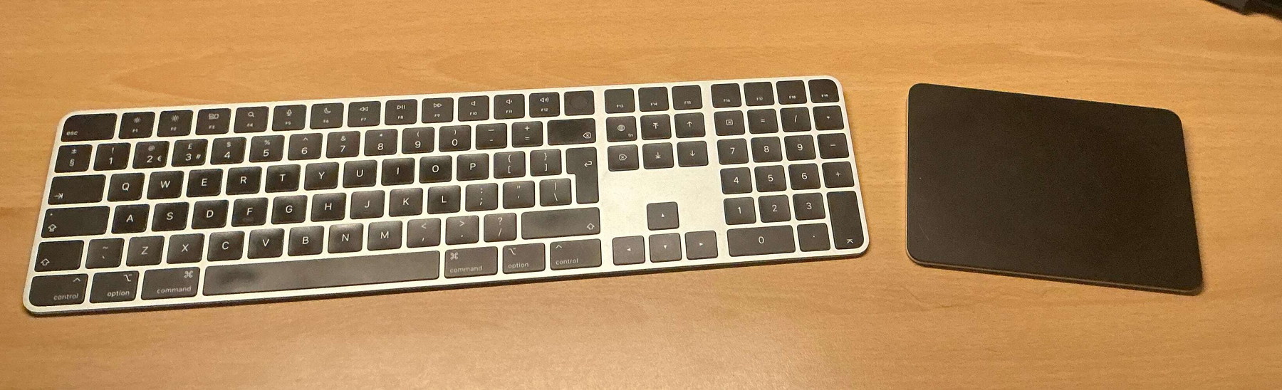 A wireless keyboard and trackpad are placed on a wooden surface.
